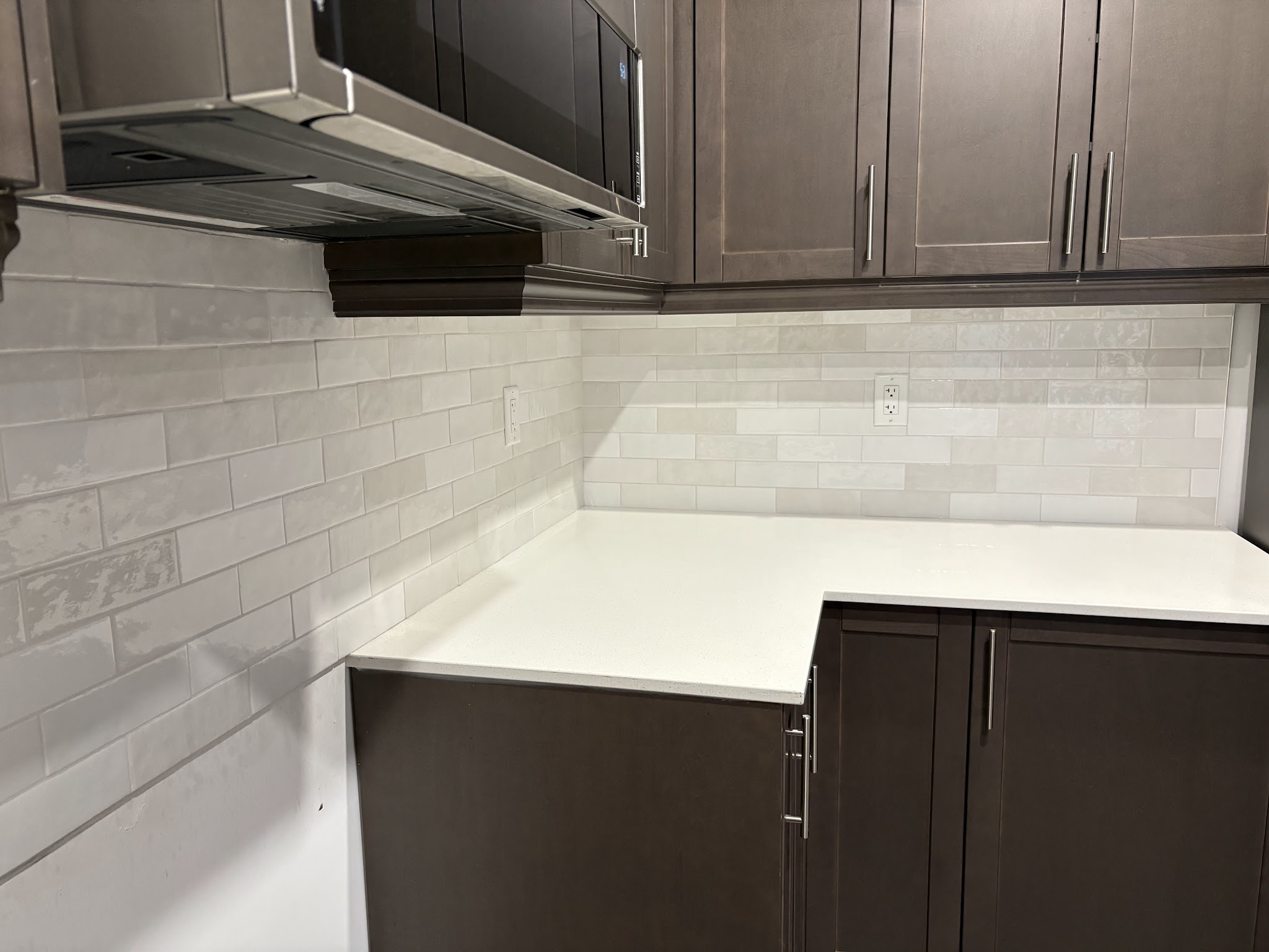 Grey subway tile kitchen backsplash under dark cabinetry with built-in microwave