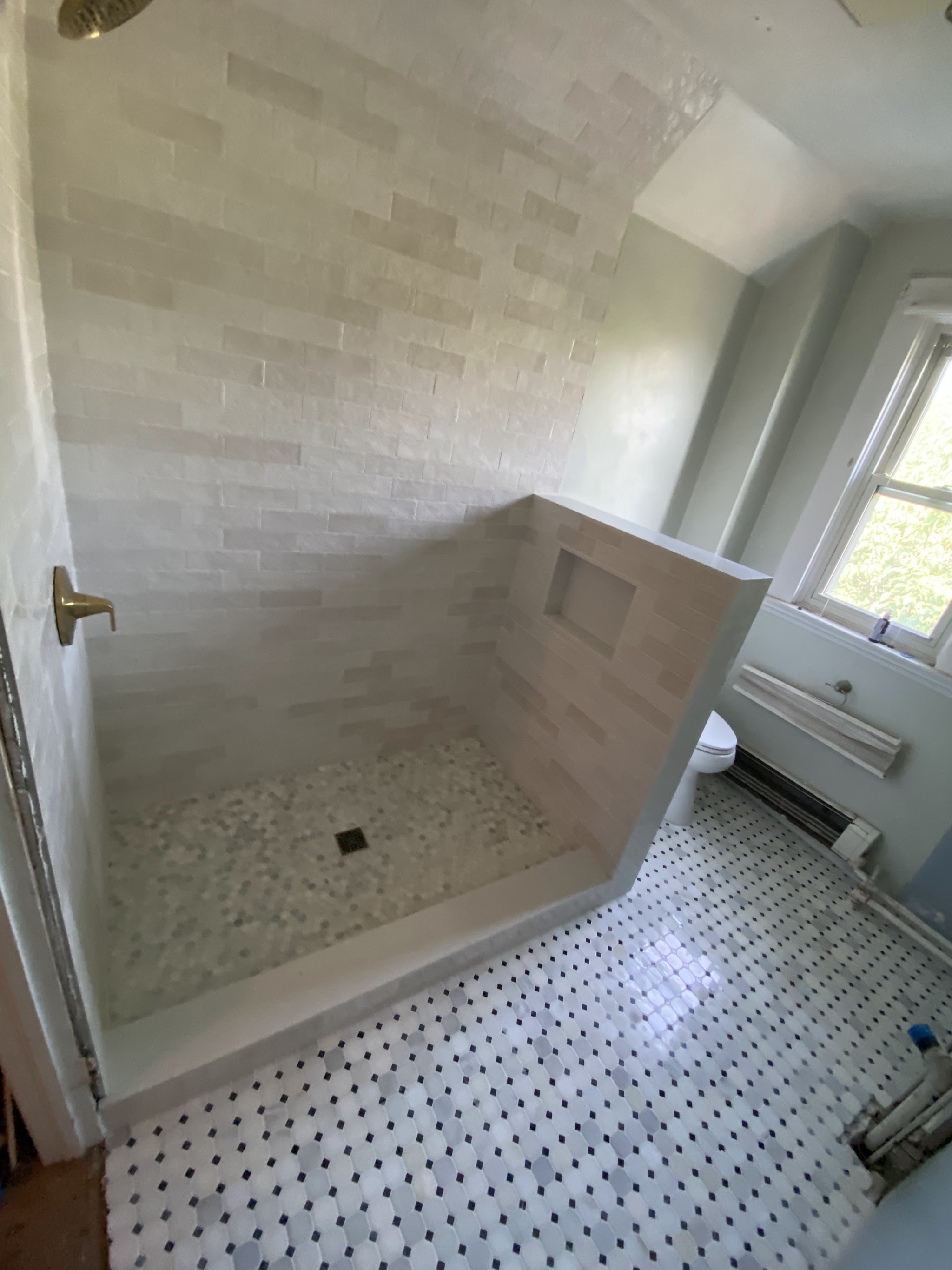 Cream subway tile shower with a half-wall niche and hexagon mosaic floor