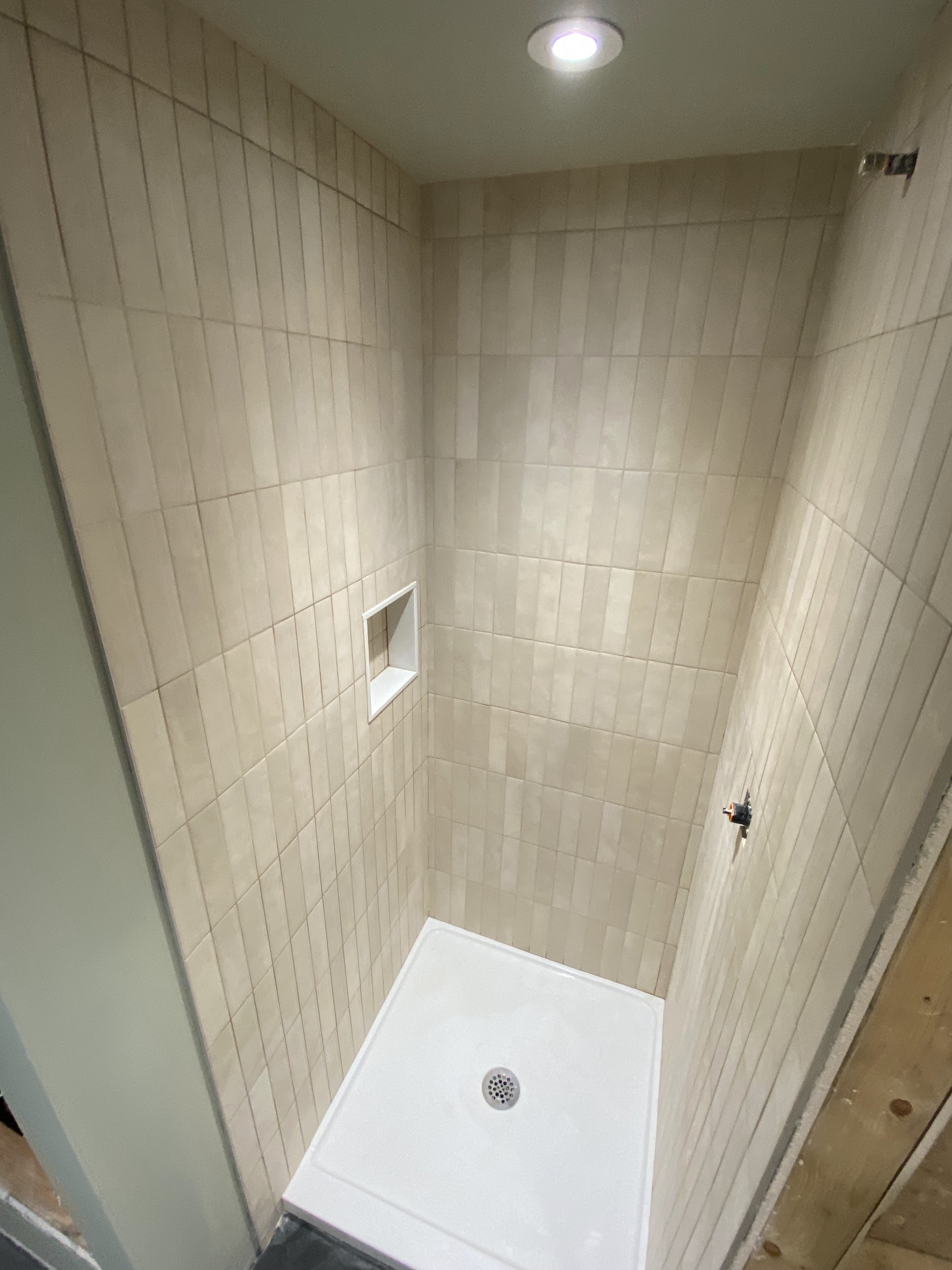 Cream vertical stack subway tile shower stall with built-in niche