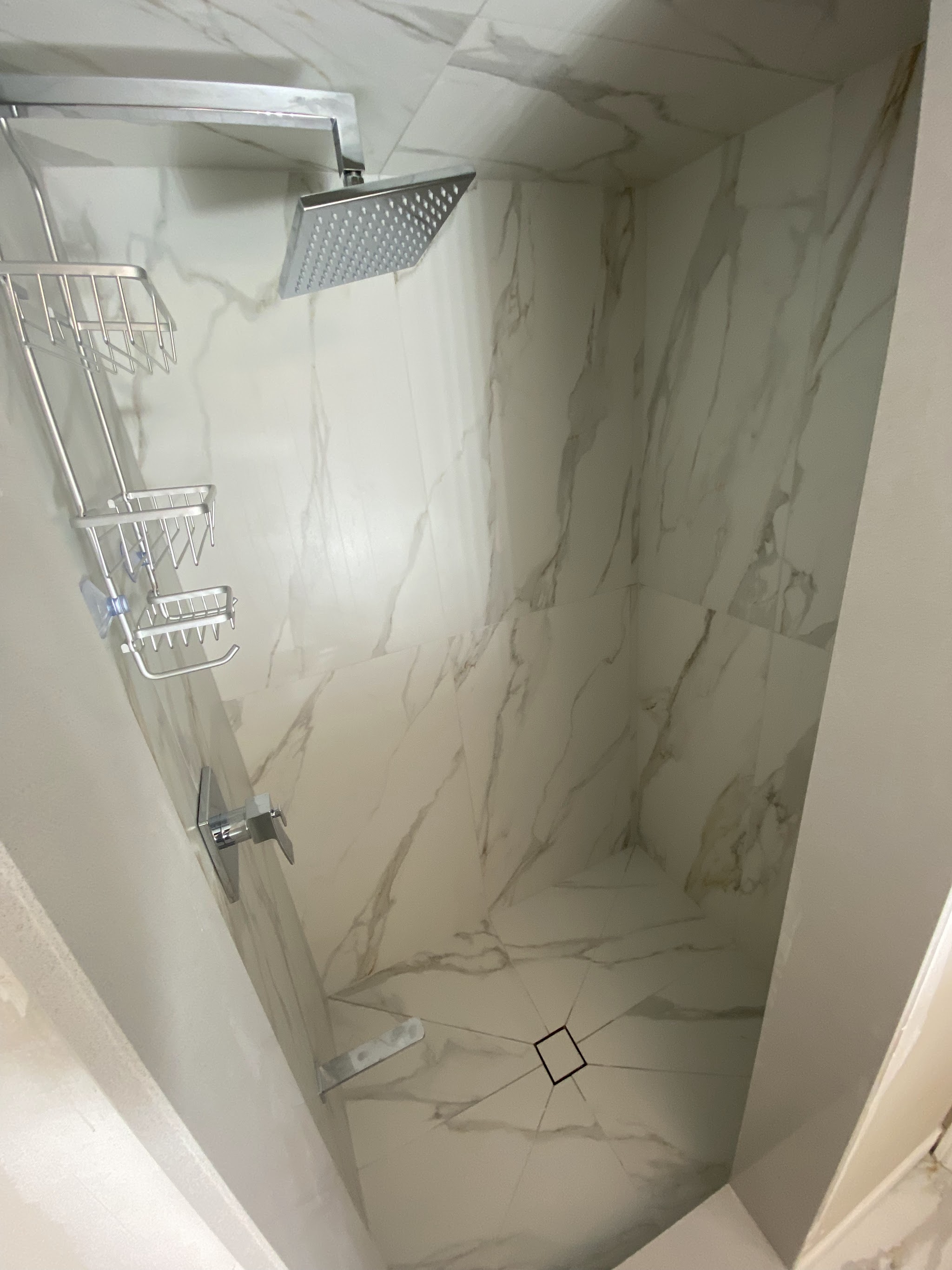 Rain shower head detail in a white marble-look shower stall with chrome caddy